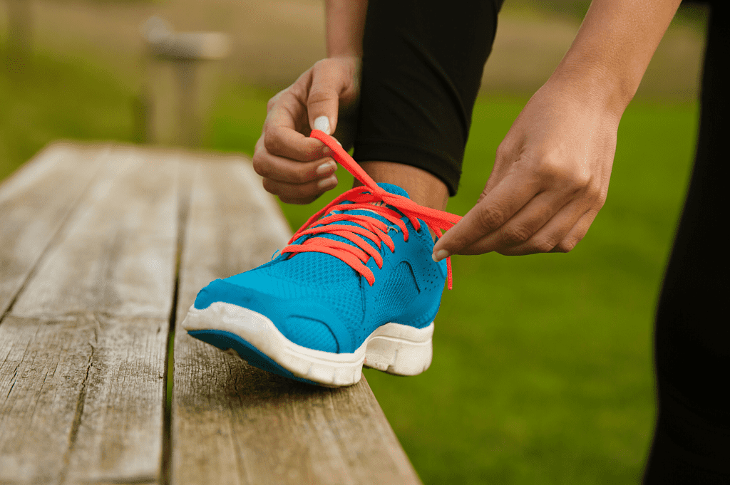 person tying red shoe lace on blue running shoe, foot on top of bench for permanent weight loss
