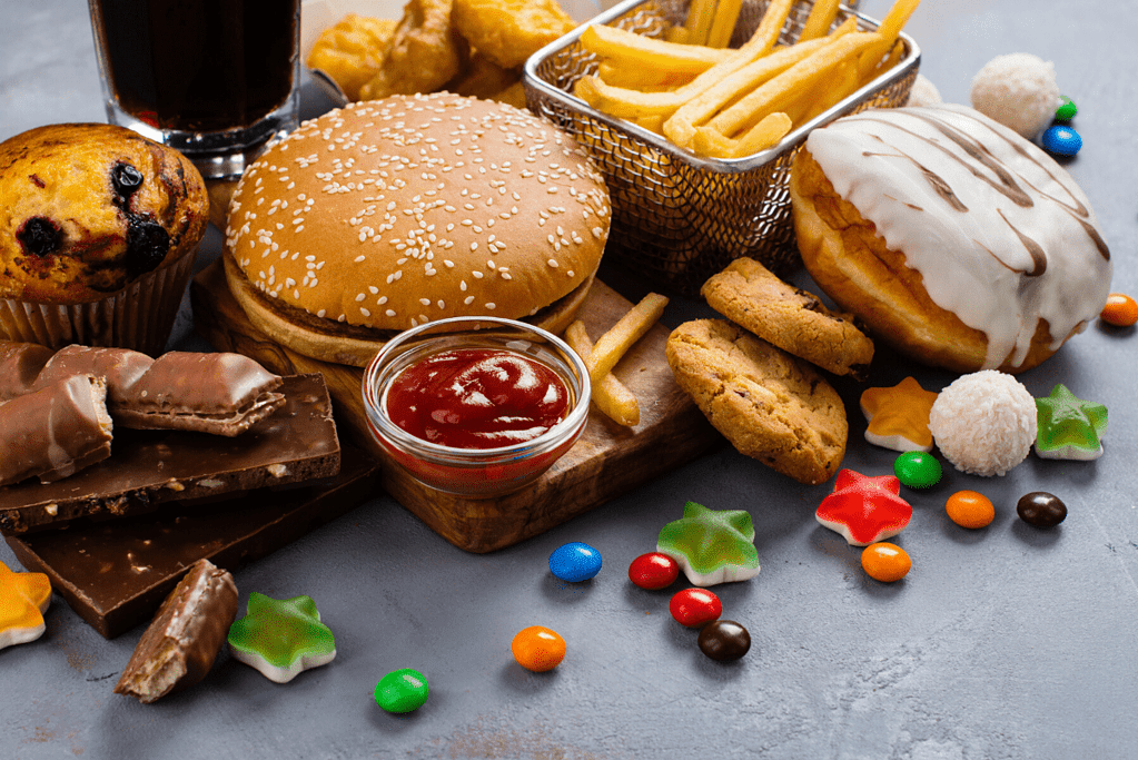 a collection of unhealthy foods for weight loss including hamburger, french fries, donut, candy, ketchup, chocolate and muffin